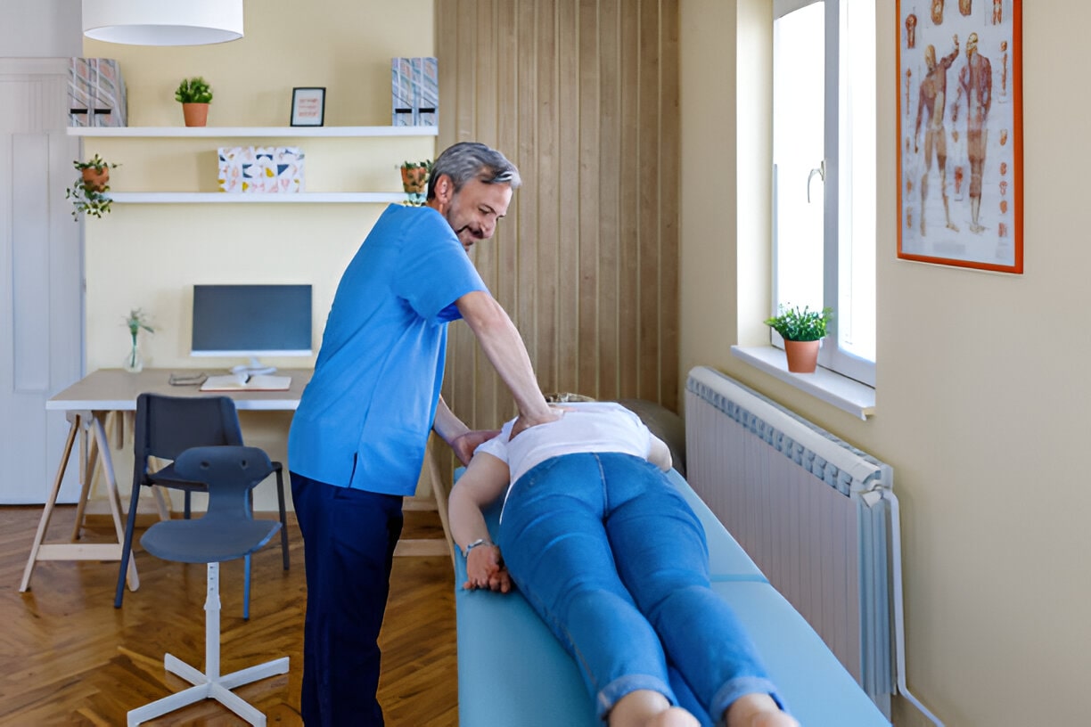 A friendly male chiropractor in St. Petersburg, FL, provides a spinal adjustment to a female patient lying face down on a treatment table. This image depicts the effective back pain relief offered by a Chiropractor St Petersburg FL.