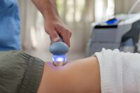 Softwave tissue regeneration technologies handheld device with glowing blue light applied to lower back during non-invasive therapy