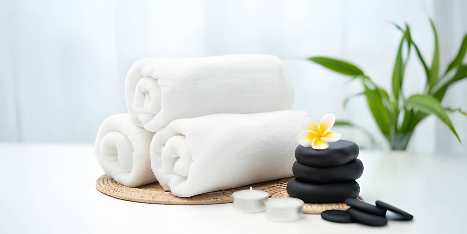 Wellness center St Petersburg FL spa arrangement with rolled towels, black stones, plumeria flower, and candles