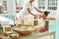 Spa aromatherapy massage with lit candles, floating flowers, scrubs, and therapist providing massage near water feature
