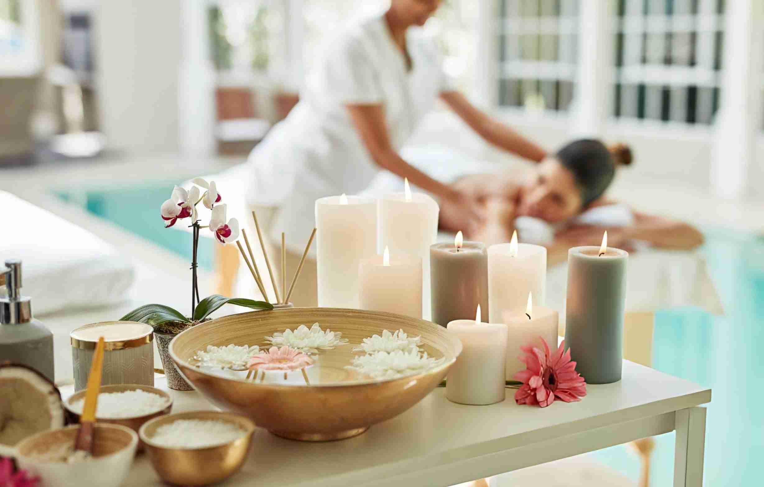 Spa aromatherapy massage with lit candles, floating flowers, scrubs, and therapist providing massage near water feature
