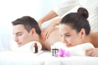 Swedish aromatherapy massage session with two clients receiving back massages using essential oils and orchid flowers in serene spa setting.