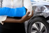 Auto Accident Chiropractor St Petersburg FL patient with arm injury standing near damaged car.