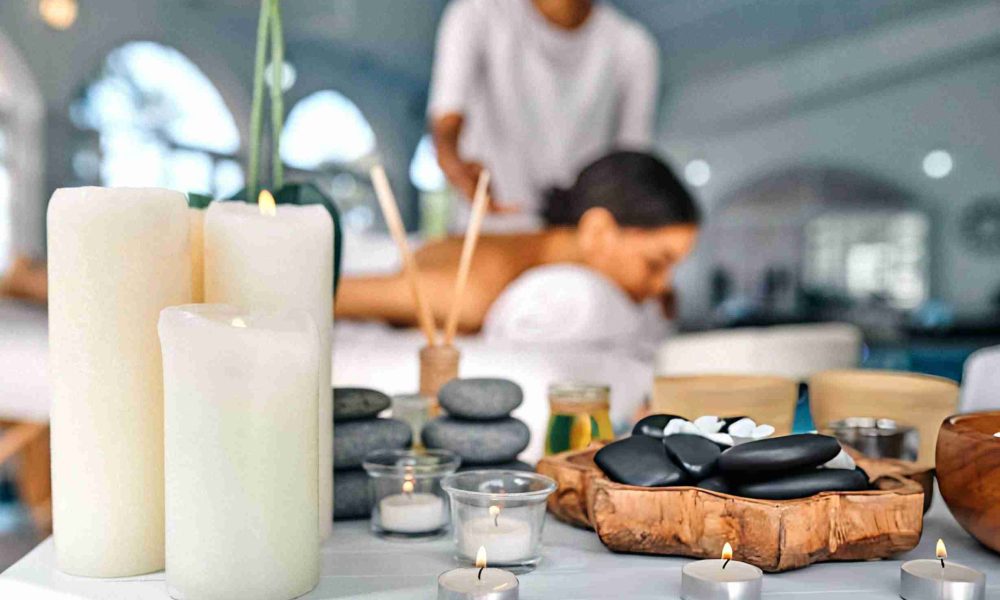 Spa aromatherapy massage with lit candles, massage stones, essential oils, and therapist providing back massage in tranquil room